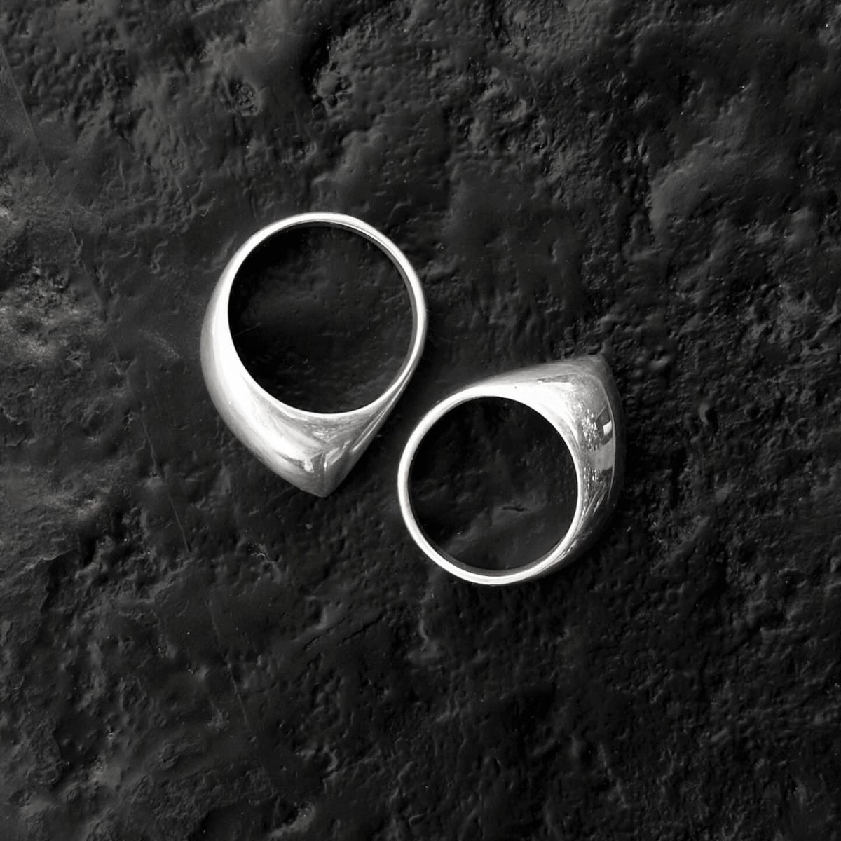 Dos anillos de sello de plata pulida sobre una superficie negra rugosa.