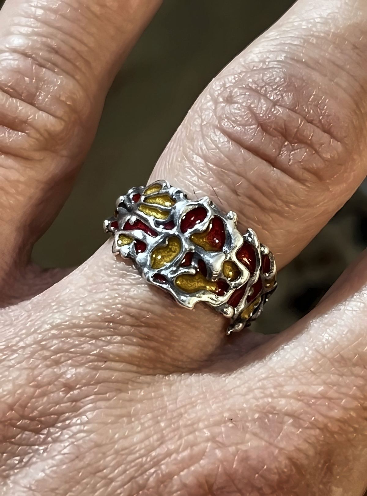 Anillo de plata con esmalte rojo y amarillo, en un dedo.