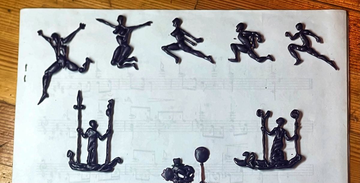 Figuras de bailarines y guerreros talladas en cera por Momik, sobre una partitura.